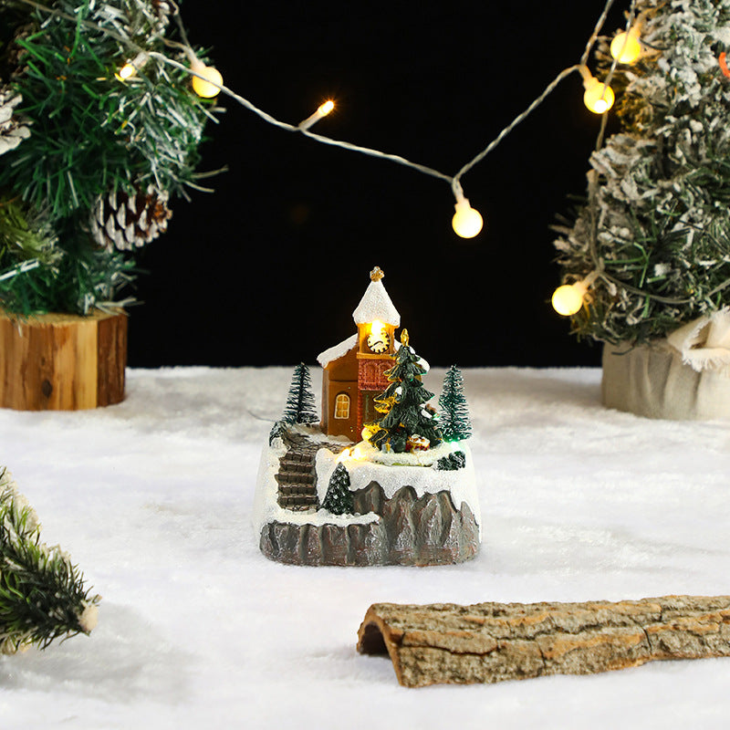 Miniature Christmas scene with a church, trees, and lights on a snowy base.