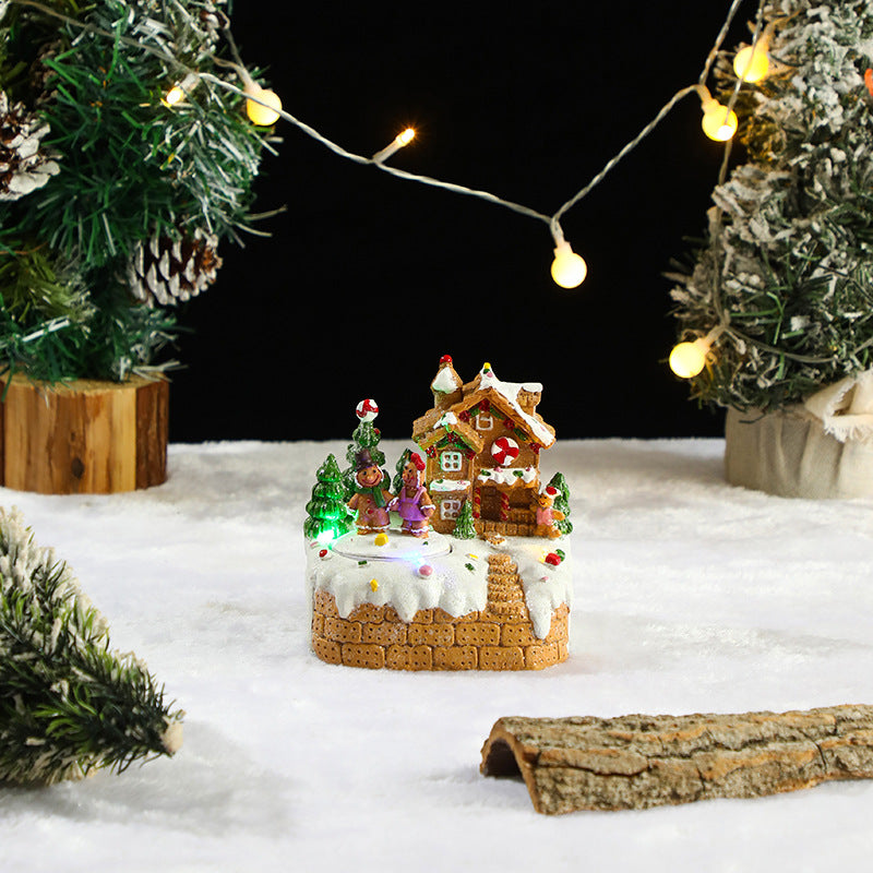 Decorative Christmas scene with a small house, trees, and lights on a snowy surface.