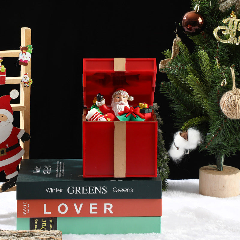 Decorative Christmas scene with a red gift box, Santa Claus figurine, and Christmas tree.