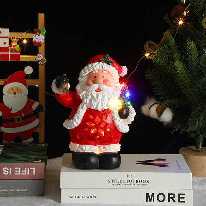 Decorative Santa Claus figure with lights on books, Christmas tree, and decorations in the background.