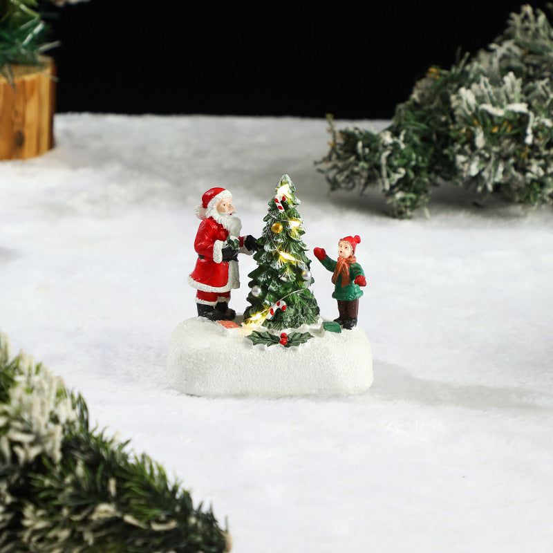 Miniature Santa Claus and child figure decorating a Christmas tree in a snowy scene.