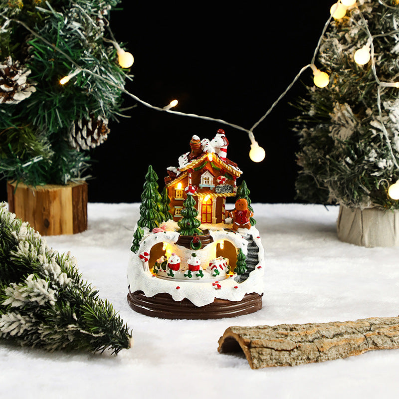 Decorative Christmas scene with a lit-up house, trees, and Santa Claus figure on a snowy base.