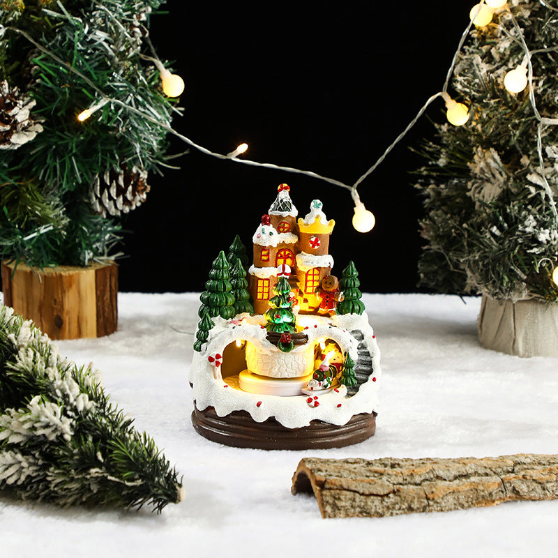 Decorative Christmas scene with a lit-up gingerbread house and trees on a snowy surface.