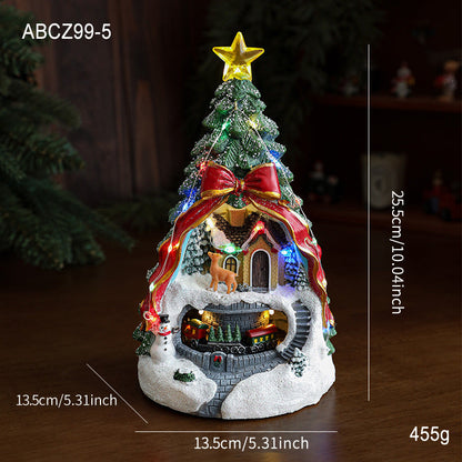 Decorative Christmas tree with a house at its base, featuring lights and a star on top, on a dark background.